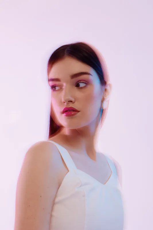 Young woman beauty fashion portrait with smooth skin and subtle makeup. She wears a white top and looks to the side against a soft pink background. Concept of elegance and style.