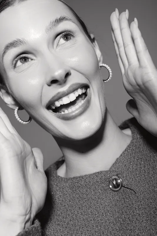 Happy Caucasian woman with light skin smiling and holding hands near face in black and white portrait.