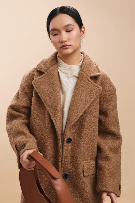 Asian woman wearing a warm wool coat stands with a handbag in a neutral studio, delivering a calm, confident, and minimalist fashion mood for contemporary campaigns and digital media.