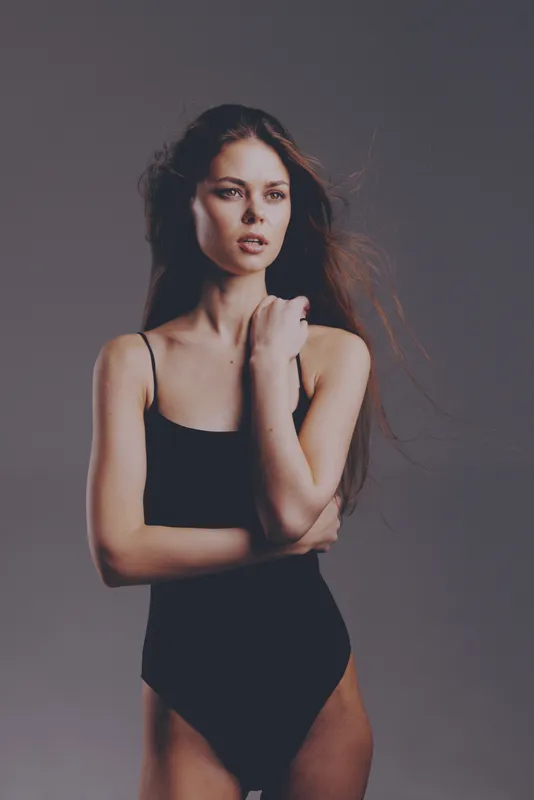serious woman posing in black bodysuit with flowing hair against neutral background, fashion, beauty, elegance