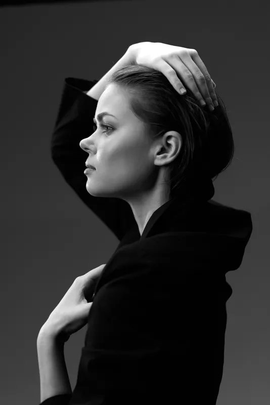 Black and white profile of a thoughtful woman in dark clothing with elegant pose and soft lighting