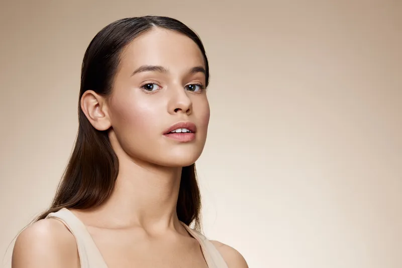 Natural beauty portrait of a young woman with smooth skin and long hair against a soft beige background, conveying serenity, elegance, and confidence