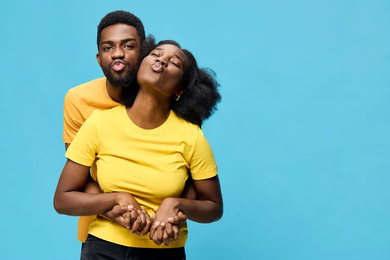 Cheerful young couple sharing a playful moment, wearing yellow shirts against a vibrant blue background, showcasing love and joy in their expressions