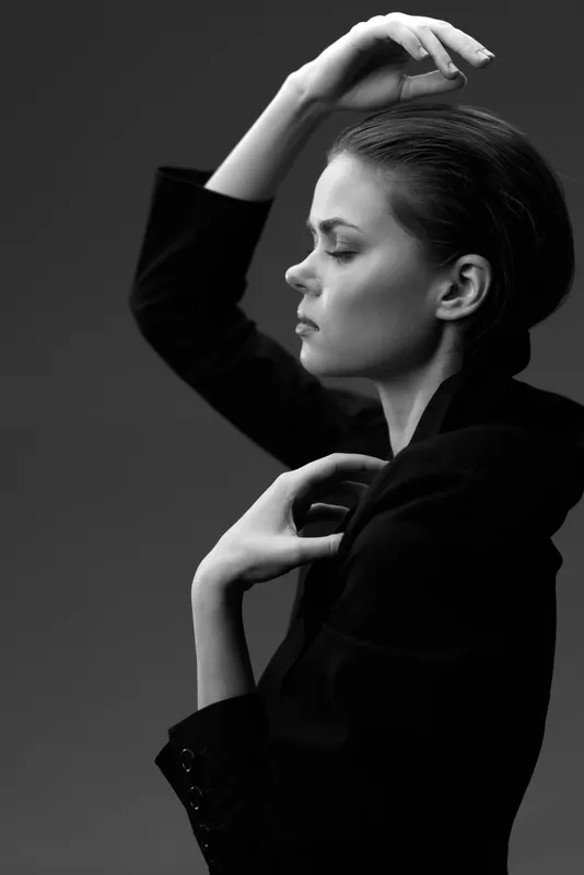 Black and white portrait of a contemplative woman in a dark jacket with a minimalist background.