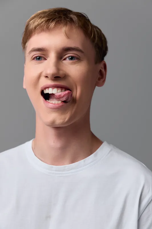 Playful moment with a young man sticking out his tongue, casual tshirt, neutral background, bright studio mood, candid expression, lighthearted humor in a modern everyday photo