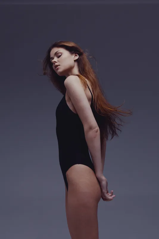 graceful woman in black bodysuit posing with closed eyes and flowing hair in studio setting