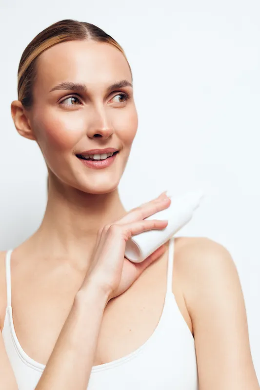 Smiling woman applies moisturizer to her shoulder, showcasing a simple skincare routine with hydration, healthy skin and a natural glow, isolated on a clean white background for stock use