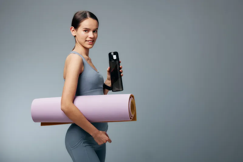 Fitness woman in athletic wear with a pink yoga mat and water bottle, ready for a workout. Sporty, healthy lifestyle portrait emphasizing training and balance.