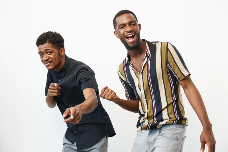 Two joyful African American men dancing together, showcasing vibrant energy and camaraderie. Their fun expressions and stylish outfits enhance the lively atmosphere.