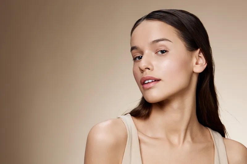 Natural beauty portrait of a young woman with smooth skin and subtle makeup against a soft beige background, exuding confidence and elegance