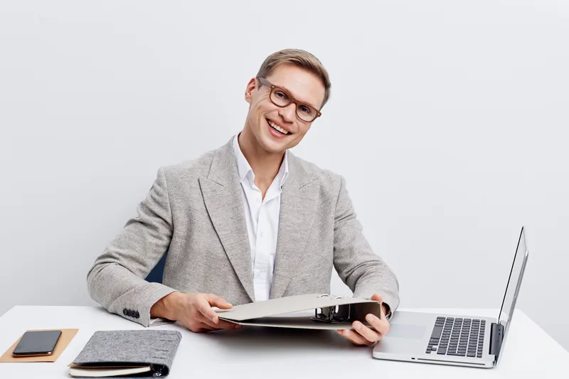 smiling man working with laptop and folder sit at table wear grey checkered blazer glasses modern digital nomad concept