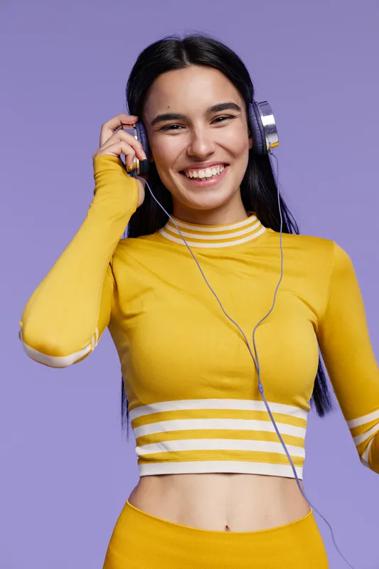young woman sport fitness smiling happily in yellow athletic wear with headphones on violet background, energetic and active lifestyle concept