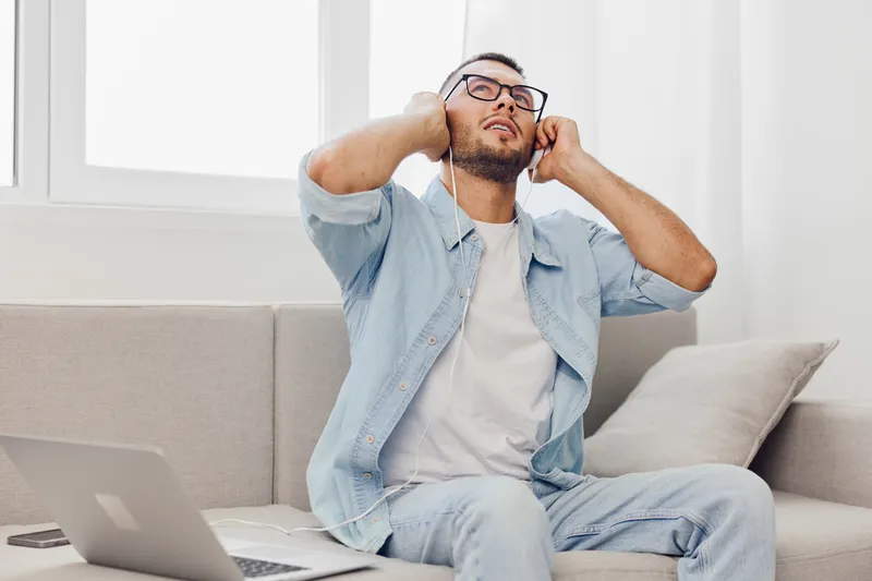 Relaxed man enjoying music while sitting on a couch, embodying a moment of tranquility and connection. Bright, modern space enhances his leisure time experience.