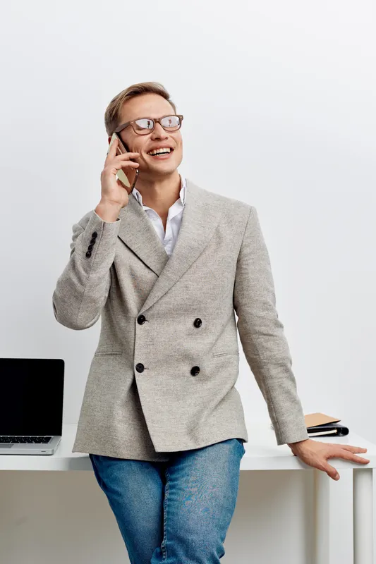 Happy confident young man in business casual attire talking on smartphone smiling while standing in modern office environment. People lifestyle concept, professional, energetic, communication, success