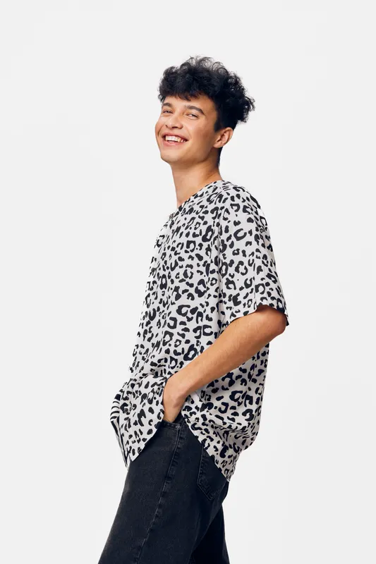 smiling man wearing leopard print t-shirt with hands in pockets standing against white background, casual style, youthful and joyful expression