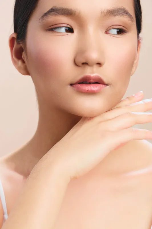 Asian woman in a closeup portrait gazes softly to the side, with a calm complexion and gentle lighting that highlights her natural beauty and thoughtful mood.