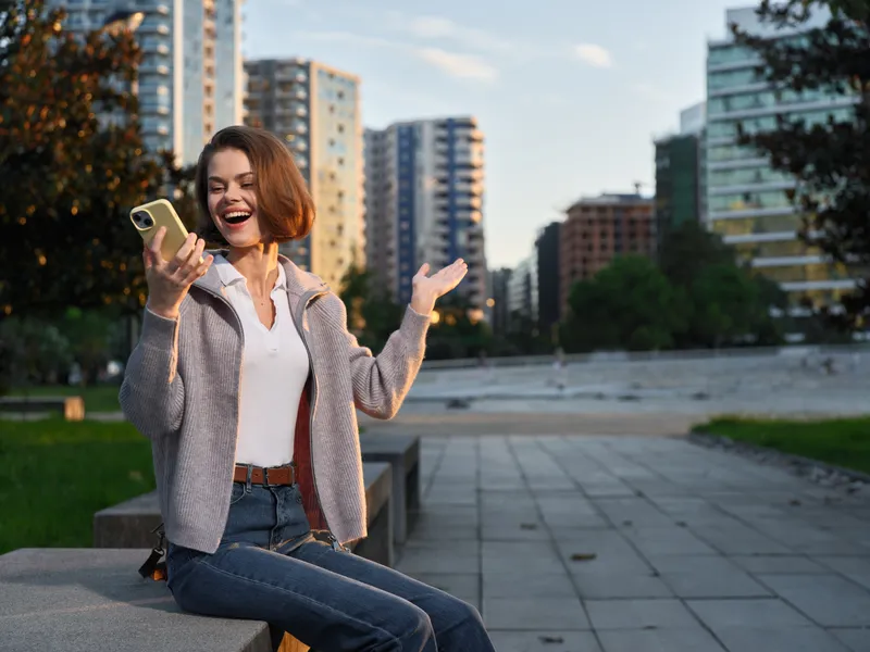 A cheerful outdoor professional is seen texting in a modern city setting. She smiles and appears engaged, creating a positive and dynamic business atmosphere.