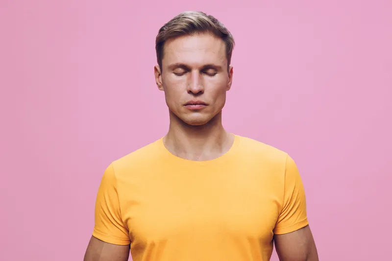 Calm man meditating closed eyes yellow t-shirt pink background mental health mindfulness wellness concept