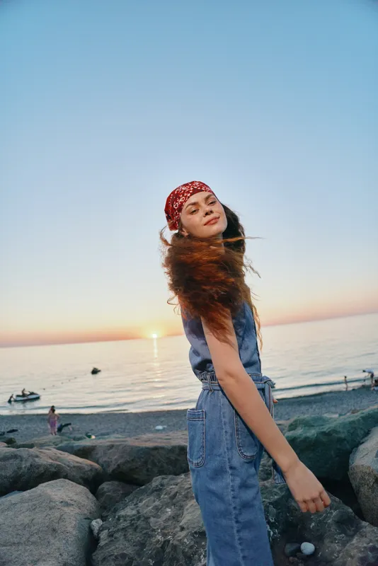 lifestyle woman in modern boho-western denim outfit enjoys sunset at the beach with relaxed street style and warm film color tones