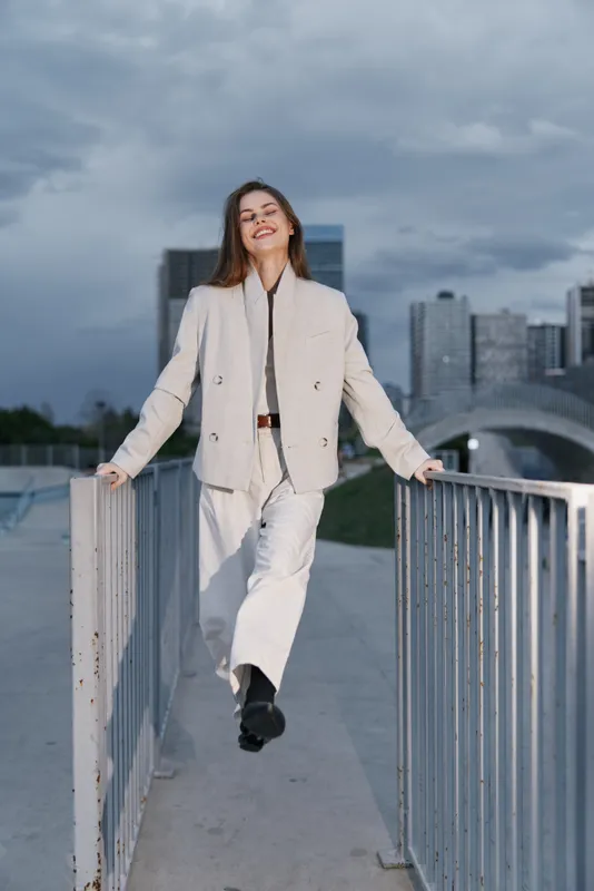 confident young woman in beige suit walking outdoors in urban city environment smiling with joy