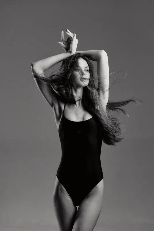 Black and white portrait of a smiling woman in a black swimsuit with flowing hair and graceful pose