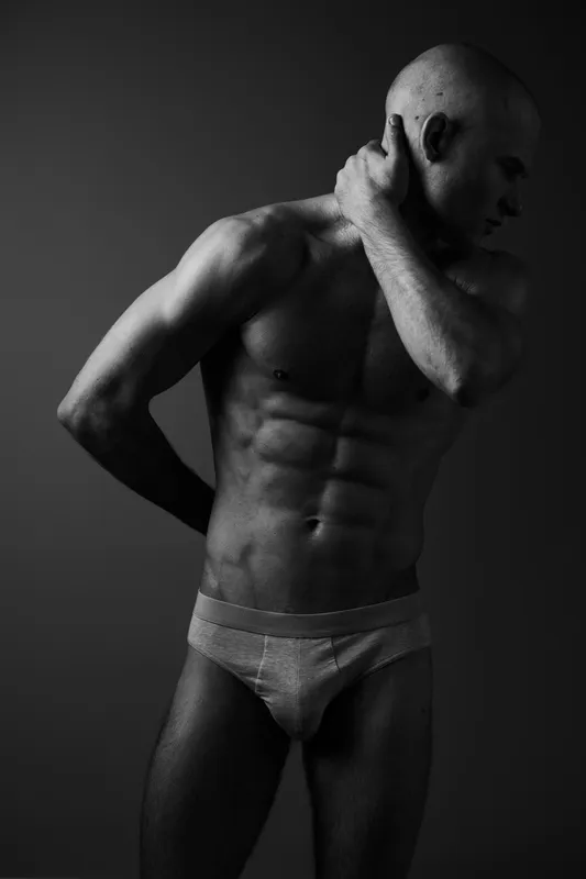 Athletic man posing in black and white, showcasing a fit physique and strong emotions. The dramatic lighting enhances the contours and features of his body.