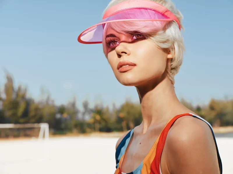 Portrait of a confident woman at the beach wearing a pink visor, bright sunlight and bold colors evoke summer fashion and outdoor freedom.