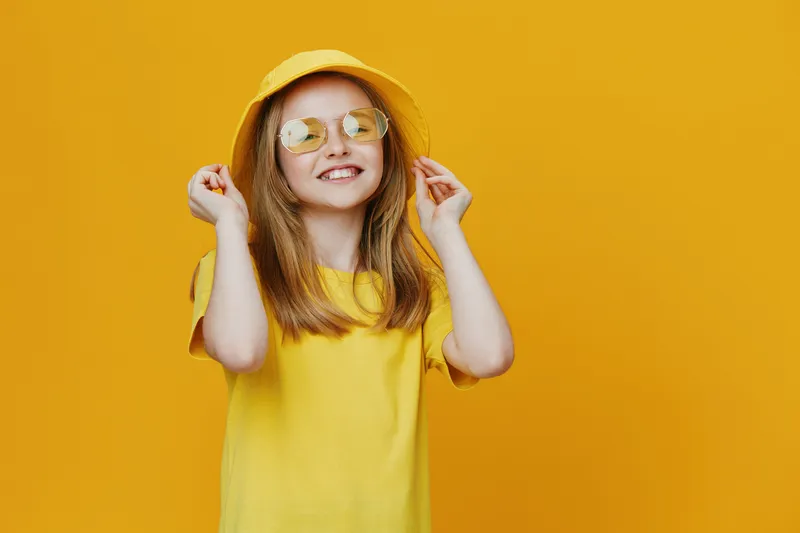 Happy girl in yellow outfit with sunglasses against a bright yellow background, embodying joy and summer vibes, perfect for children s fashion and playful themes