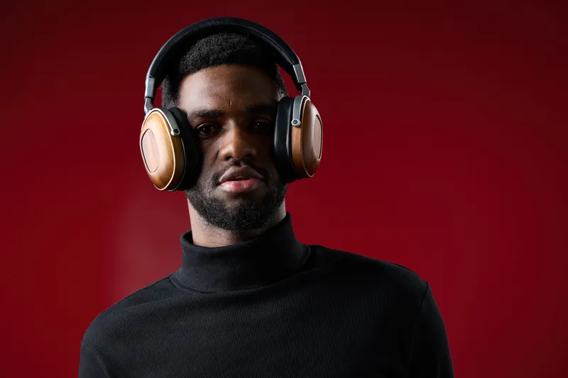 Young Black man wearing stylish headphones against a vibrant red background, showcasing modern fashion and confident expression
