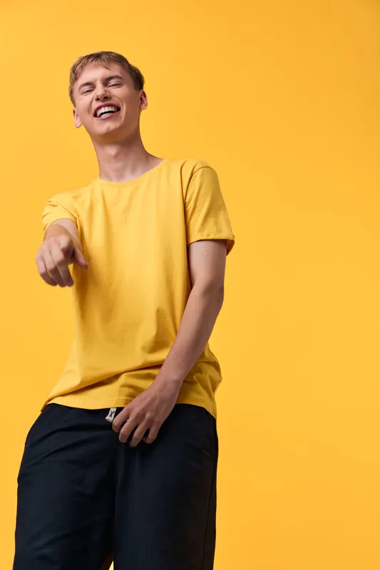 Cheerful man in a yellow tee laughing and pointing forward against a bright yellow backdrop, dynamic studio shot highlighting casual style, energy, and confident, playful gesture.