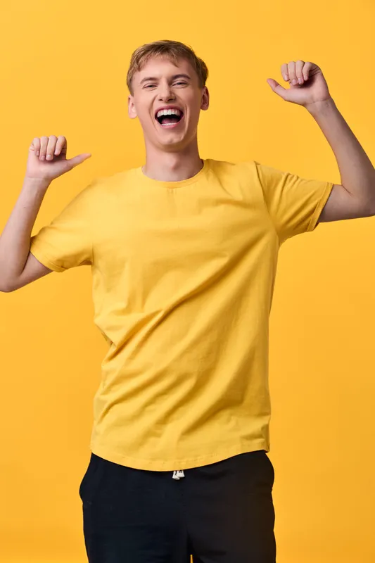 Happy, energetic man celebrates with raised arms in a bright yellow shirt against a vibrant backdrop, conveying joy, energy, and positive mood for promotional use