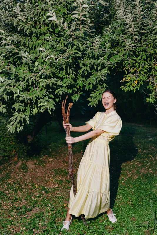 Woman in yellow dress joyful under tree in nature authenticity inclusivity outdoors smiling with stick and sunlight
