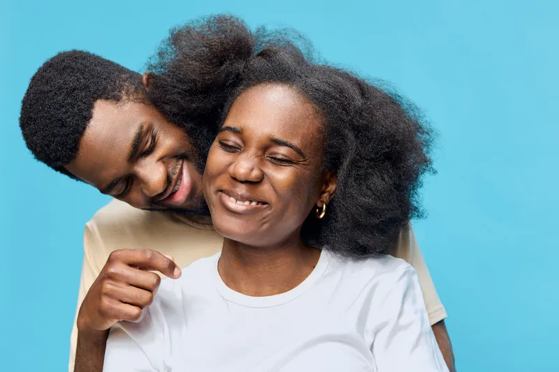 Joyful couple with natural hair smiling against a bright blue background, showcasing love and connection in a warm and vibrant atmosphere