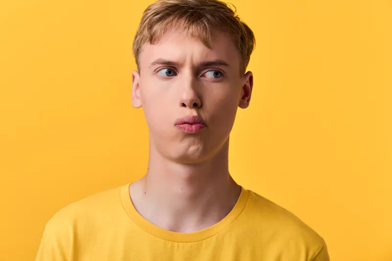 Pensive youth man with a puzzled expression under a bright yellow backdrop, wearing a matching yellow shirt, conveying curiosity and contemplation in a minimal studio shot
