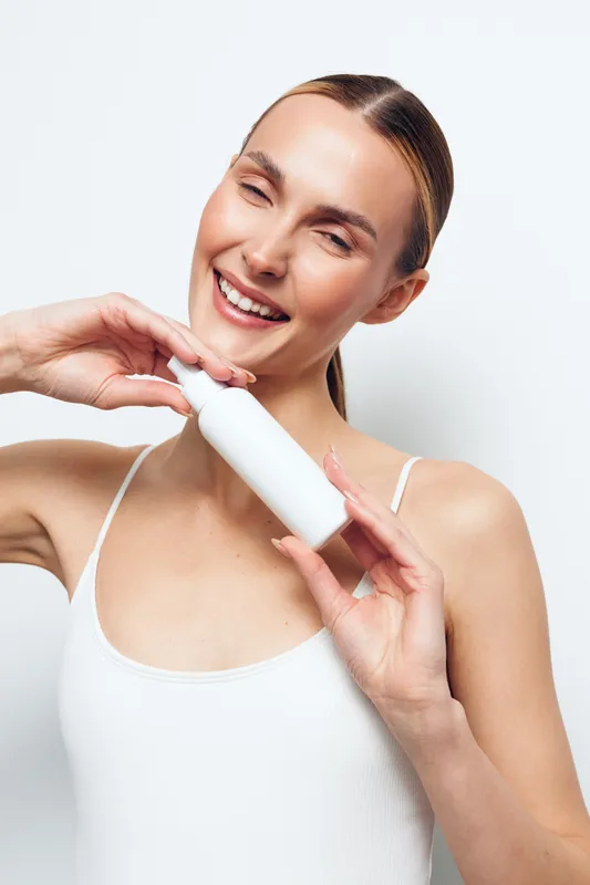 Woman skincare beauty facial cream self care hygiene wellness concept, smiling young woman applies moisturizer to her cheek with a white applicator on a clean light background, close view for