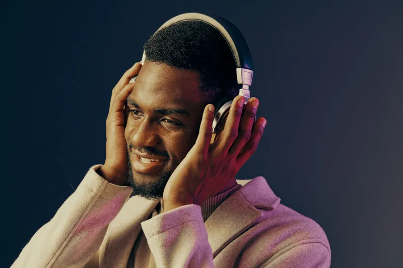 A joyful man wearing headphones and a stylish light jacket, immersed in music against a colorful gradient background, reflecting modern lifestyle and emotions