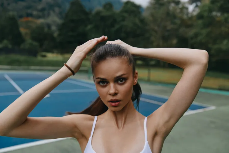 Young athletic woman adjusting her ponytail on a tennis court, exuding confidence and determination amid a vibrant green background