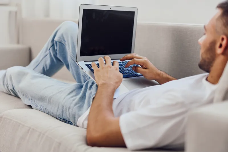 A relaxed man with a laptop rests comfortably on a couch, embracing modern work-life balance while enjoying a casual workspace at home.