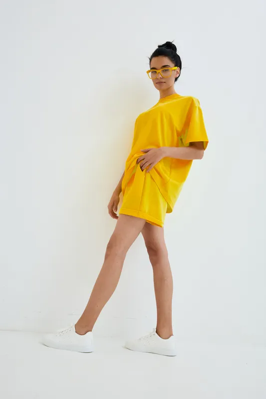 young woman in bright yellow outfit and matching sunglasses posing confidently against white minimalistic background, casual style, summer fashion look
