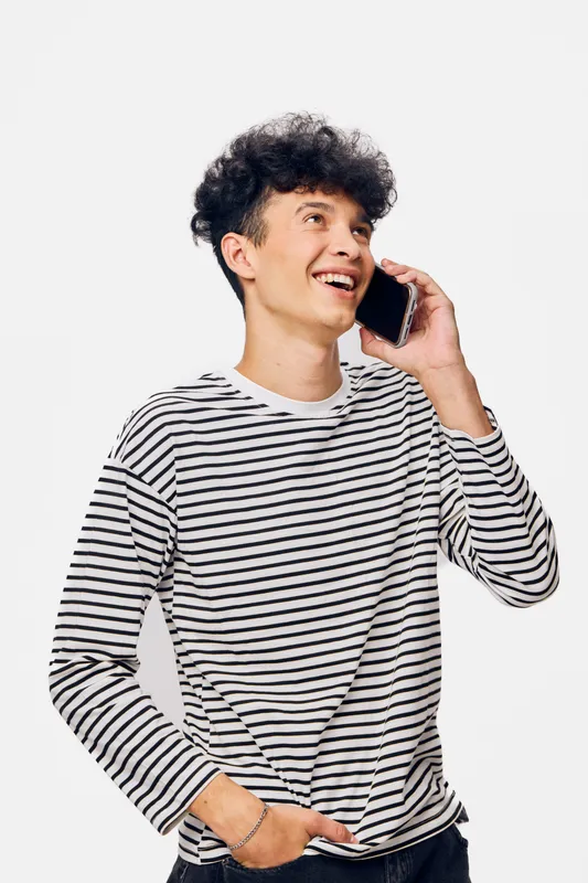 young man talking on smartphone wearing a striped shirt, smiling with joy, casual style, isolated white background, modern communication concept
