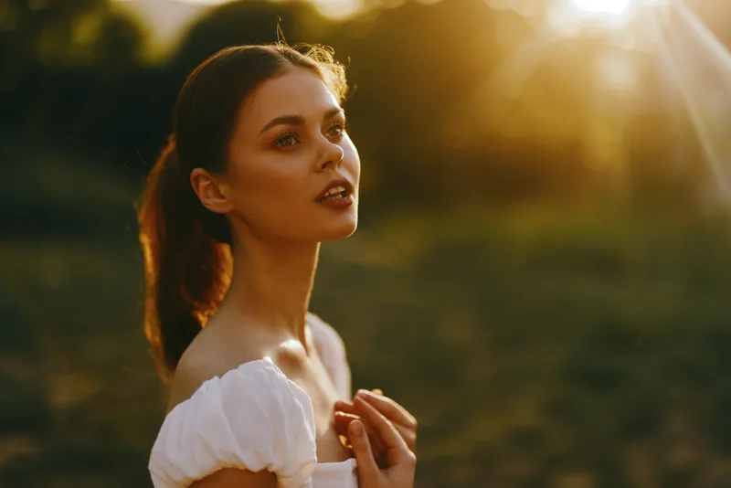 Young woman in a white dress enjoys a sunset, expressing serenity and contemplation, surrounded by nature