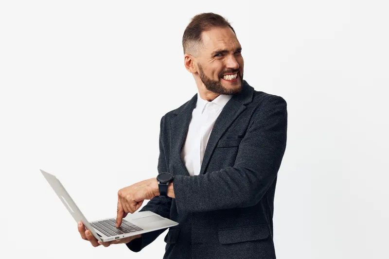 A professional businessman stands on an isolated white background, exuding confidence while using a laptop and presenting a strong, positive emotion.