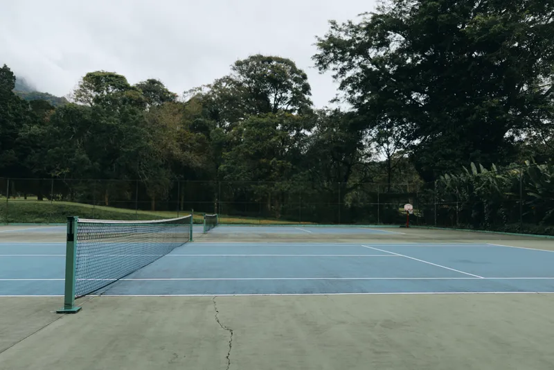 Empty tennis court surrounded by greenery reflecting a calm and serene atmosphere, ideal for promoting sports and outdoor activities