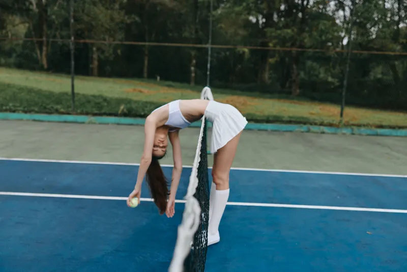 Young female tennis player stretching near the net on a sunny day, embodying athleticism and focus in a vibrant outdoor setting