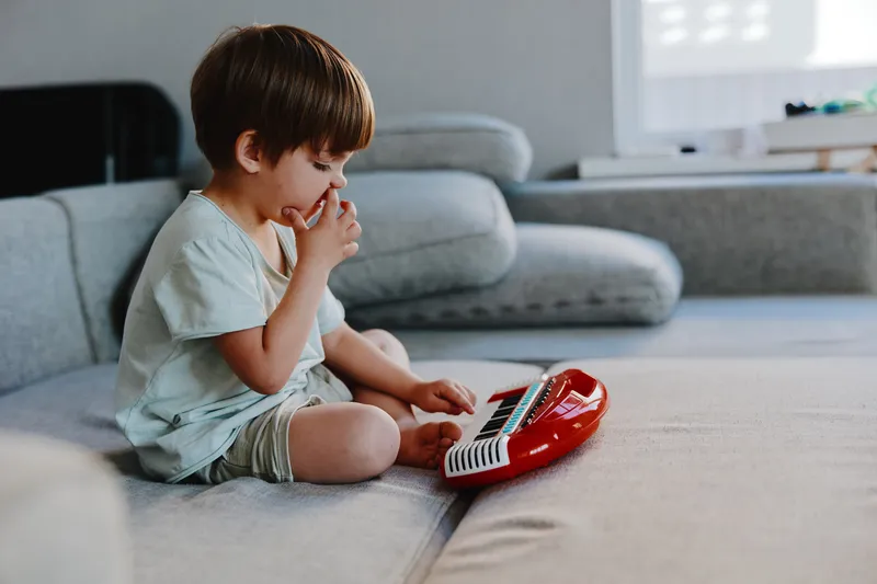 Creative boy playing music on a red keyboard at home, immersed in sound and joy. This delightful scene captures childhood imagination and musical exploration.