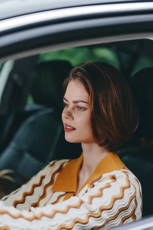 Portrait of a young woman seated in a car, calm and composed, with soft natural light highlighting her thoughtful expression.