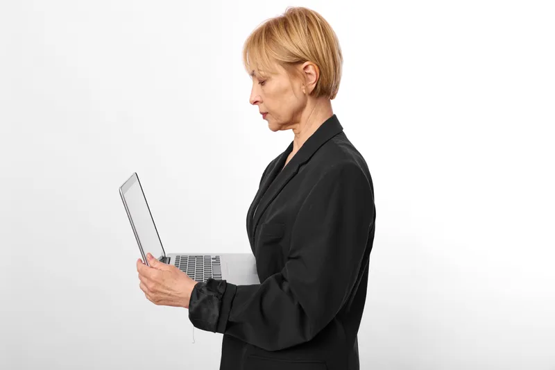 Elderly woman in business attire holding a tablet, side profile portrait in a studio setting, white background, focused expression, neutral colors, modern technology concept