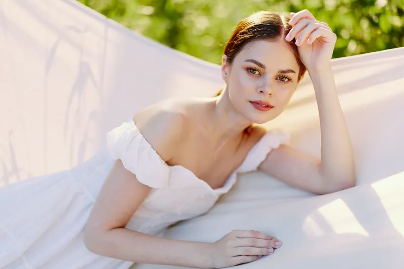 Beautiful young woman in a white dress lounging on a hammock, radiating calmness and serenity amidst a lush green background