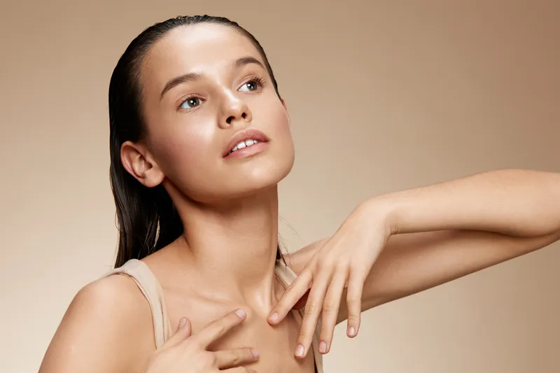 Young woman with fresh skin and elegant pose, showcasing natural beauty and confidence against a soft beige background, perfect for skincare and beauty concepts