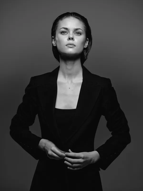 Serious woman in black blazer with confident expression, black and white portrait with dramatic lighting.